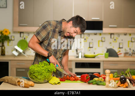 Vue avant de l'homme debout dans la cuisine couper des légumes, peur grimace Banque D'Images