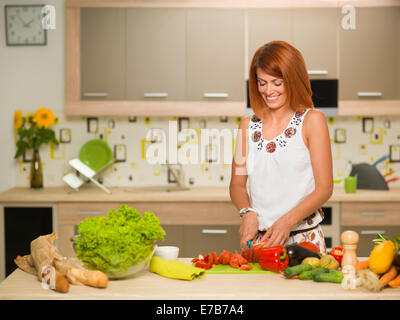 Vue avant du young Beautiful woman femme debout dans la cuisine, couper des légumes et souriant Banque D'Images