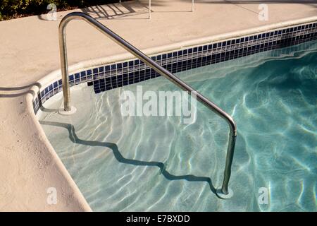 Des marches et une main courante chromée mènent dans le bleu de l'eau d'une piscine Banque D'Images