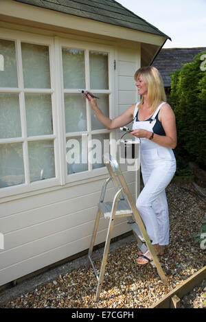 Peintre décorateur peinture fenêtres d'un bureau de jardin debout sur un escabeau Banque D'Images