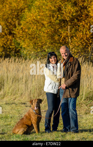 Cheerful couple avec chien dans park autumn sunset Banque D'Images