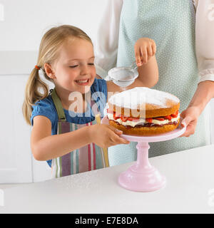 Smiling girl tamisant le sucre à glacer sur une fraise éponge, 5 ans Banque D'Images