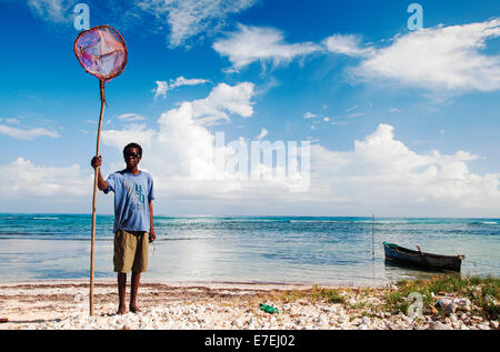 La JAMAÏQUE. Un homme maigre est titulaire d'un filet de pêche à la main comme il se dresse sur une plage vide nommé "succès.' un petit canot flotte dans une eau bleue. Banque D'Images