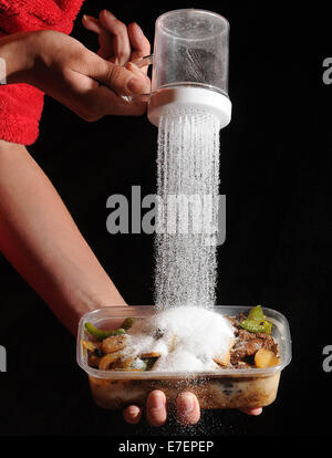 Une femme verse du sel sur un repas à emporter malsaine. Banque D'Images