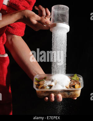 Une femme verse du sel sur un repas à emporter malsaine. Banque D'Images