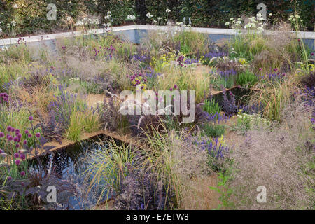 Anglais moderne jardin de gravier avec l'eau caractéristique piscine plantation d'herbes ornementales alliums plantes en croissance lits de fleurs jardin frontière été Royaume-Uni Banque D'Images
