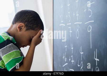 Mixed Race boy faire des problèmes de mathématiques à bord en classe Banque D'Images