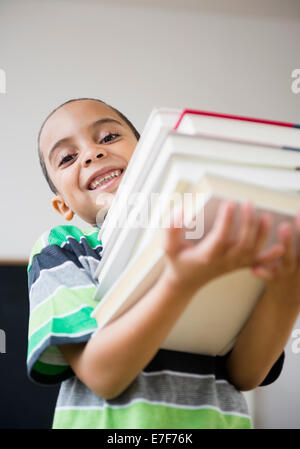 Mixed Race boy carrying pile de livres dans la classe Banque D'Images