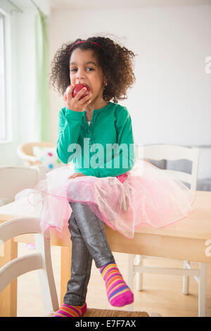 African American girl eating apple à la table de cuisine Banque D'Images