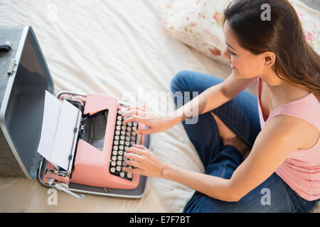 Femme à l'aide de machine à écrire sur le lit Banque D'Images