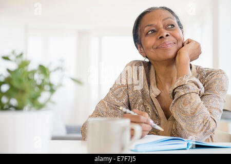 Mixed Race woman writing at desk Banque D'Images