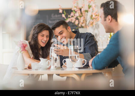 Amis hispaniques using cell phone in cafe Banque D'Images