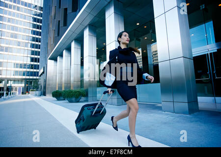 Mixed Race businesswoman rolling bagages enregistrés en ville Banque D'Images