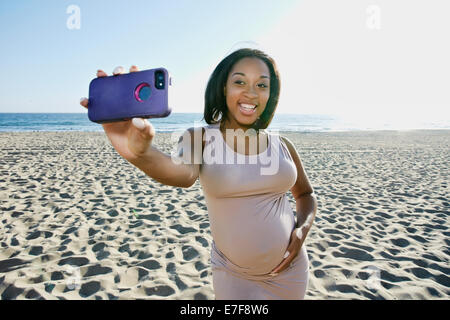 Femme enceinte de prendre cell phone photo on beach Banque D'Images