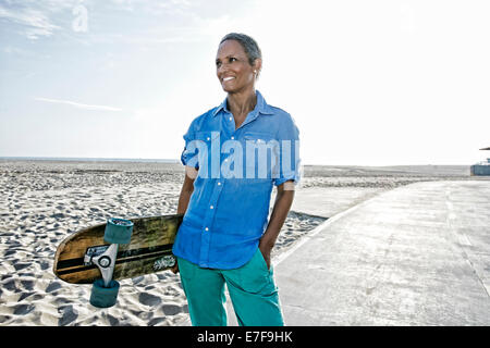Older black woman holding skateboard on beach Banque D'Images