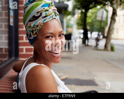 Black woman sitting on bench on city street Banque D'Images