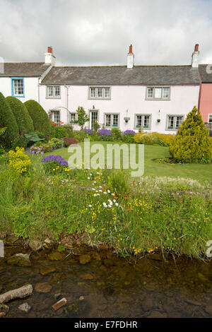 Cottage Anglais peint en blanc avec jardin soigné, pelouse, des masses colorées de fleurs de printemps et petit cours d'eau au village de Caldbeck dans Cumbria Banque D'Images