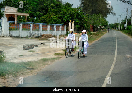 Deux des étudiants du secondaire riding bicycles on rural road, portant la traditionnelle Ao Dai. Cu Chi, Vietnam Banque D'Images