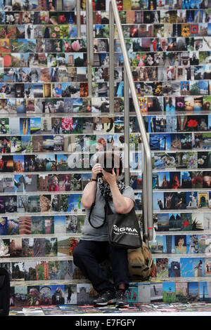 Femme assise sur un escalier couvert de milliers de photos, Photokina 2014, Cologne, Allemagne Banque D'Images