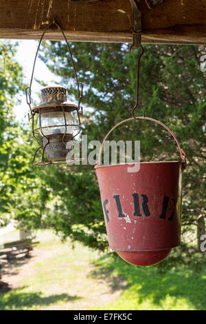 Ancien seau incendie usés et lampe à pétrole suspendue à chevrons de log cabin Banque D'Images