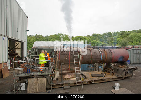 Vêtements haute visibilité avec des ouvriers à l'atelier de chemin de restauration de la locomotive à vapeur historique avec de la fumée s'échapper de chaudière Banque D'Images