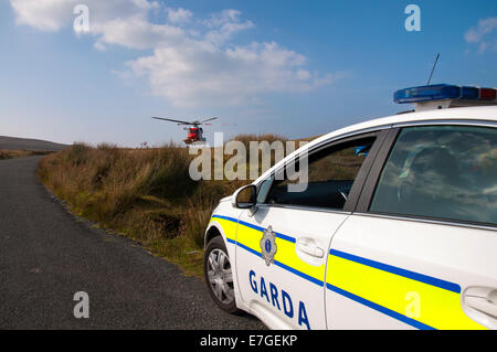 La Garde côtière irlandaise IRCG Garda Cósta na hÉireann hélicoptère Sikorsky vole au-dessus d'une voiture de police irlandais lors d'un secours médical Banque D'Images
