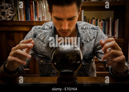 Beau jeune homme, la prévision de l'avenir en regardant dans une boule de cristal noir Banque D'Images