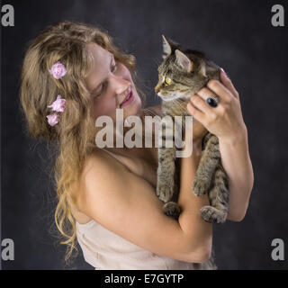 Fille mignonne avec roses dans ses cheveux et avec un chat sur ses mains Banque D'Images