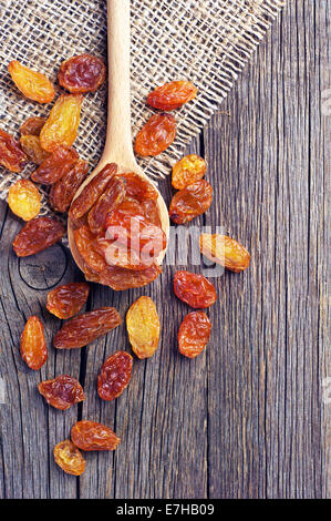 Les raisins secs dans une cuillère en bois sur fond de bois vintage Banque D'Images