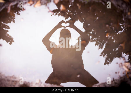 Reflet dans une flaque d'une personne qui forme un coeur avec ses mains. Banque D'Images