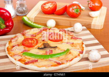 Smiling pizza sur une planche à découper et des légumes frais Banque D'Images