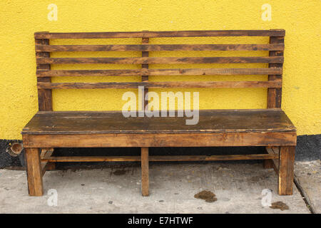 Un banc de parc en bois à côté d'un mur de béton jaune à Cotacachi (Équateur) Banque D'Images