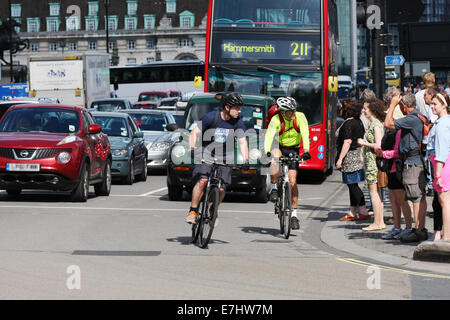 Deux cyclistes se déplacer hors d'une série de feux de circulation en face d'une file d'attente de trafic. Attendre les piétons de traverser la route. Banque D'Images