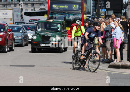 Deux cyclistes se déplacer hors d'une série de feux de circulation en face d'une file d'attente de trafic. Attendre les piétons de traverser la route. Banque D'Images