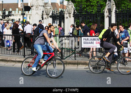 Deux cyclistes voyageant autour d'un coude en place du Parlement, Londres. les gens marchent sur la chaussée. Banque D'Images