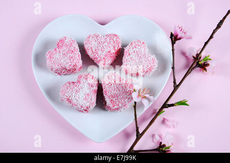 Style australien fait maison en forme de coeur rose petit gâteau Lamington sur plaque blanche en forme de coeur Banque D'Images