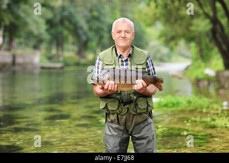 Pêcheur matures debout dans River et la tenue d'un poisson à l'extérieur Banque D'Images