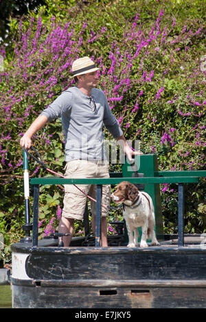 Homme et chien de compagnie sur un bateau étroit narrowboat traversant les écluses de Caen Hill sur le canal Kennet et Avon, Devizes, Wiltshire, Angleterre, Royaume-Uni en août Banque D'Images