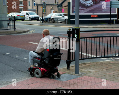 Man sur la mobilité scooter, crossing road à pedestrinl crossing, Barrow-in-Furness Cumbria, Angleterre, Royaume-Uni Banque D'Images