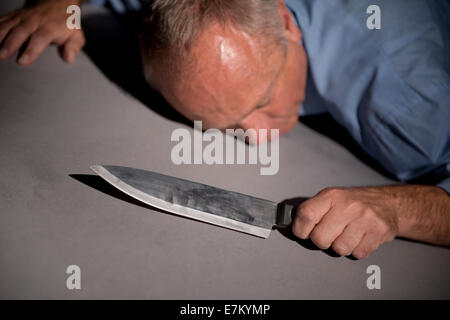 Vue oblique d'un homme, allongé sur le sol, tenant un couteau de cuisine. Banque D'Images