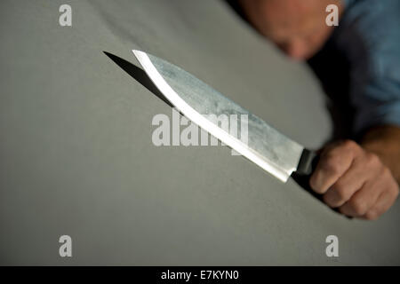 Vue oblique d'un homme, allongé sur le sol, tenant un couteau de cuisine. Banque D'Images