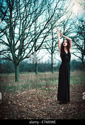 Un mignon goth girl wearing robe noire se dresse parmi les arbres d'automne Banque D'Images