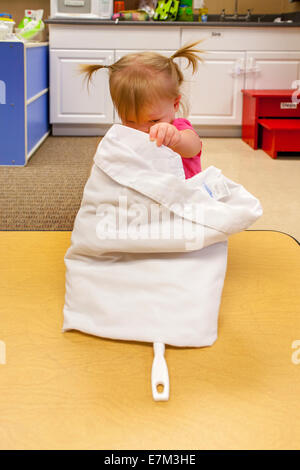 Montrant la curiosité, un bébé fille atteint sous un chiffon pour trouver un jouet dans une garderie à Tustin, CA. Banque D'Images