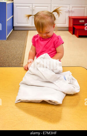 Montrant la curiosité, un bébé fille atteint sous un chiffon pour trouver un jouet dans une garderie à Tustin, CA. Banque D'Images