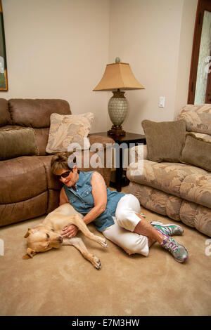 À la maison dans la banlieue de Irvine, CA, une femme aveugle joue affectueusement avec son chien-guide Labrador Retriever jaune Banque D'Images