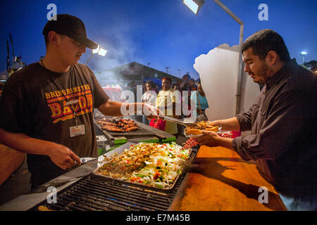 Hispanique un client achète une saucisse grillée et légumes d'un vendeur de fast-food à l'Orange County Fait à Costa Mesa, CA. Remarque T shirt chocolat publicité bacon. Banque D'Images