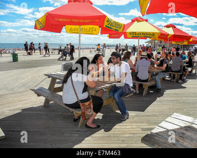 Les sections locales multiraciales profitez d'une journée ensoleillée sur la promenade à Coney Island, New York. Remarque Les parapluies de la célèbre Nathan's restaurant. Banque D'Images