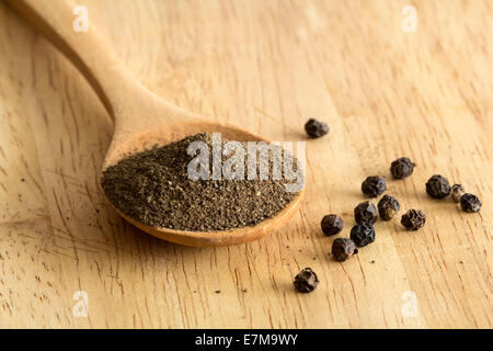 Tas de poudre de poivre noir sur une cuillère en bois et le poivre en grains, faible profondeur de champ Banque D'Images