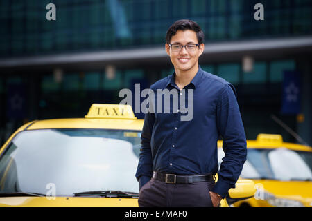 Portrait of happy chinese chauffeur de taxi s'appuyant sur voiture jaune avec les bras croisés, souriant et looking at camera Banque D'Images