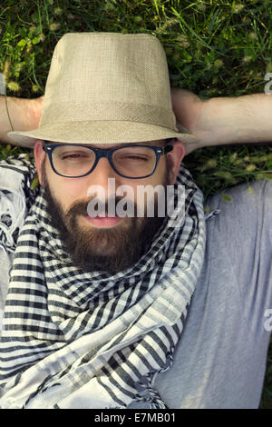 Portrait of a smiling young man hipster barbu allongé dans l'herbe et la rêverie Banque D'Images